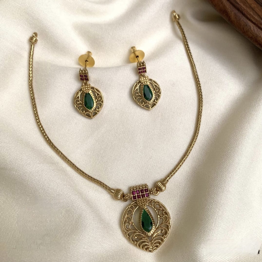 Gold necklace and earrings with green and red stones on a white fabric background
